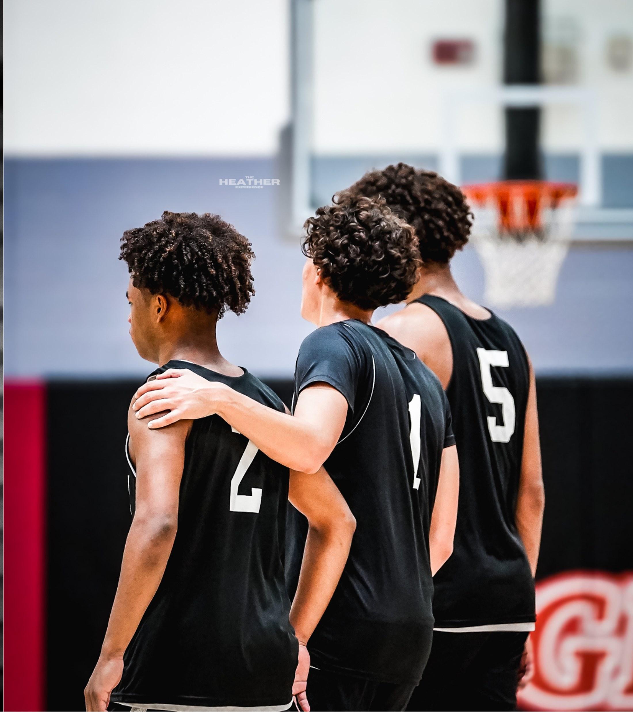 Three teammates walking onto the court together, arms around each other's shoulders, seen from behind.