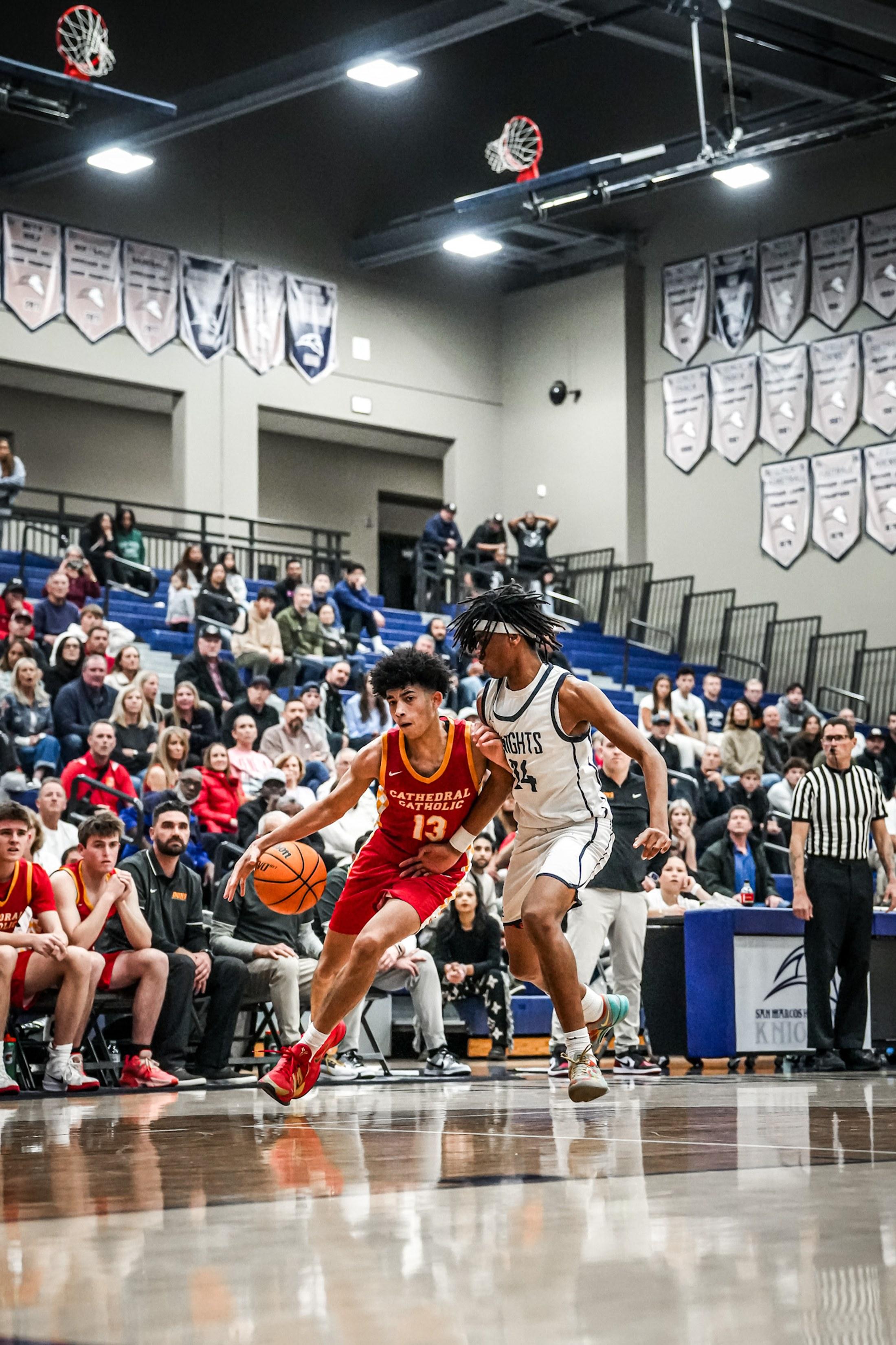 A basketball player driving to the basket past a defender, playing full-out in front of a packed crowd.