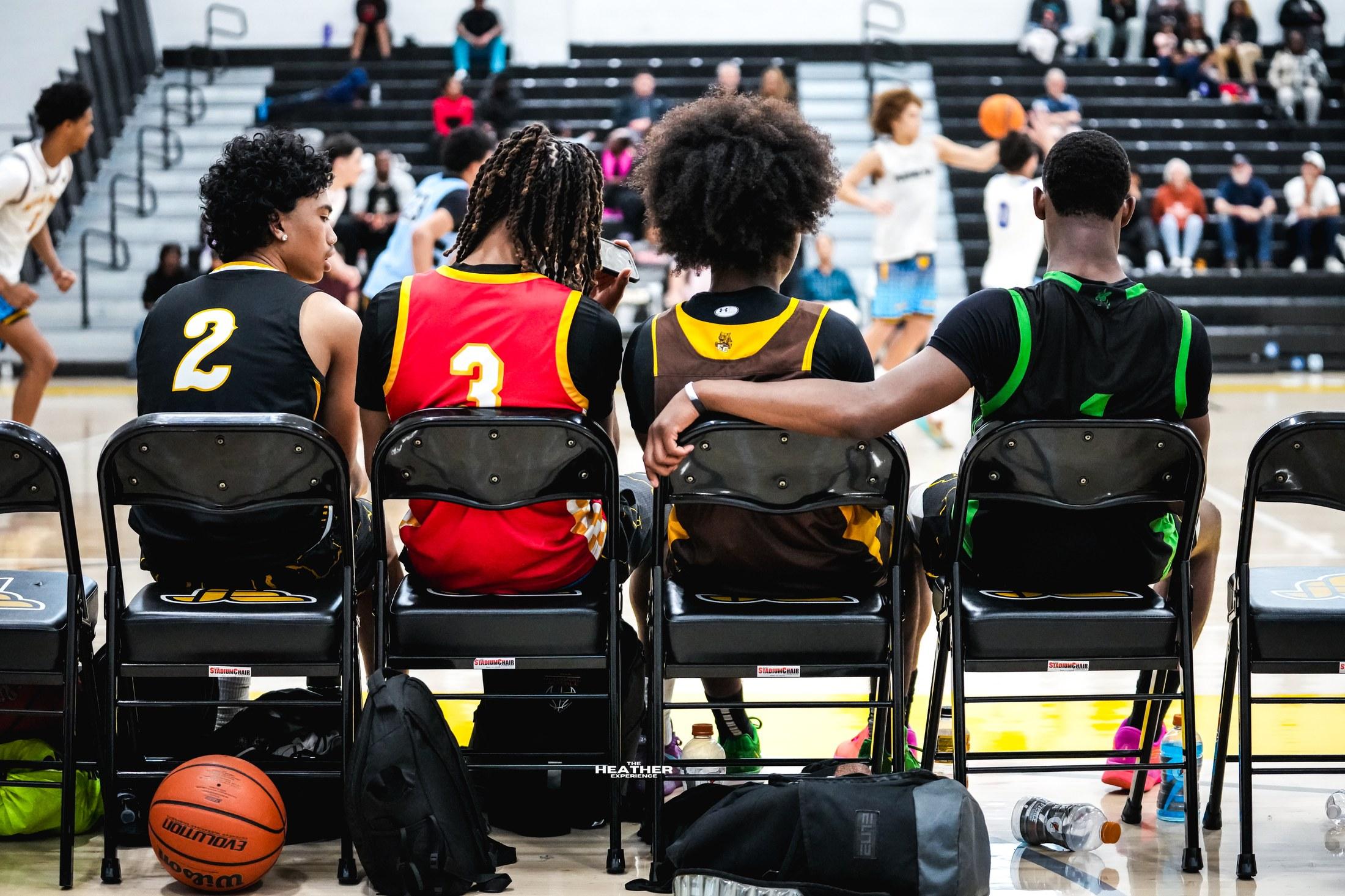 Four teammates seen from behind, sitting together on the bench, one with an arm around the next.